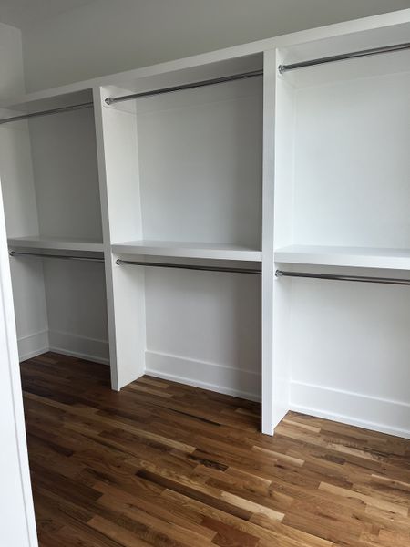 A spacious walk-in closet with sleek white shelving and warm hardwood flooring.