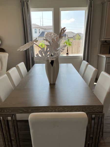 A modern dining room with a sleek wooden table, white chairs, and large windows opening to a backyard view.