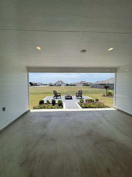 A spacious covered patio leading to a landscaped seating area with Adirondack chairs and stone path.