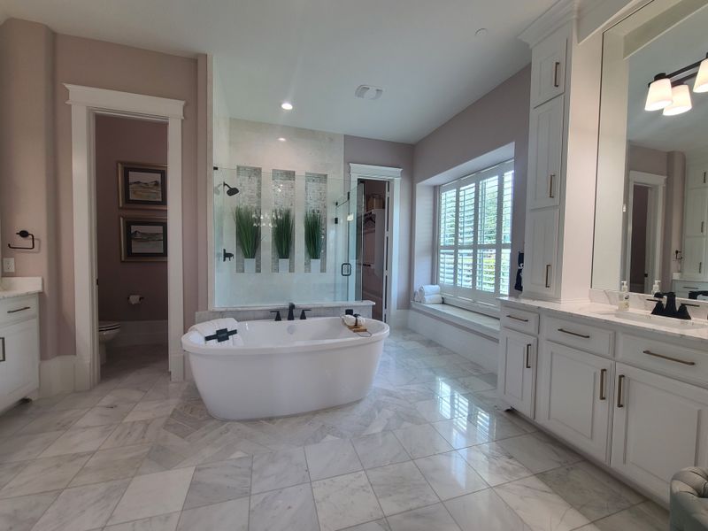 A luxurious bathroom featuring a freestanding tub, marble floors, ample cabinetry, and a large window seat. A luxurious bathroom featuring a freestanding tub, marble floors, ample cabinetry, and a large window seat.