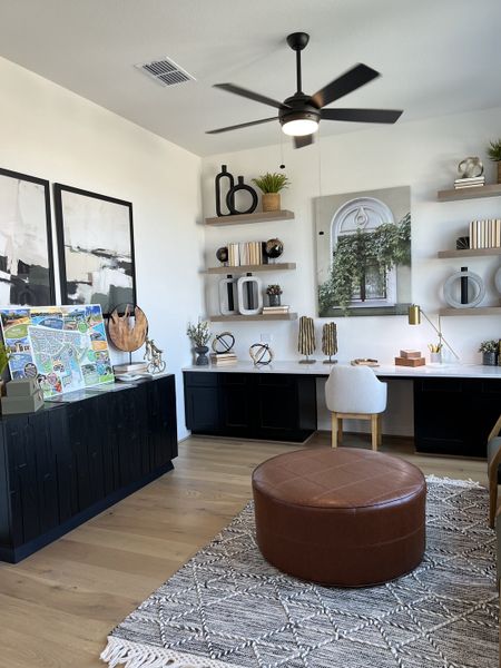 A stylish home office with chic shelving, modern artwork, a ceiling fan, and cozy leather seating. A stylish home office with chic shelving, modern artwork, a ceiling fan, and cozy leather seating.