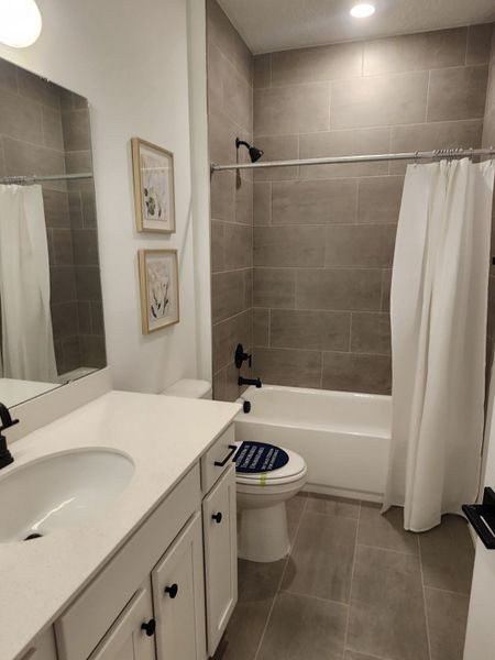 A modern bathroom featuring taupe tiled walls, sleek black fixtures, and a white vanity with ample storage.