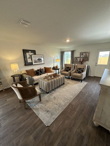A cozy living room with a plush sofa, armchairs, soft lighting, and elegant decor on a warm-toned wooden floor.