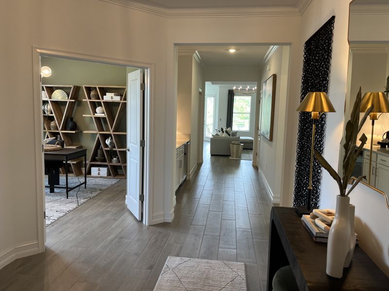 A modern hallway with sleek wood floors, a chic office, and stylish decor accents leading to a bright living area.