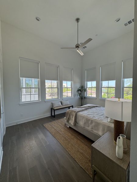 A bright bedroom with large windows, cozy rug, sleek gray flooring, and modern decor, featuring a ceiling fan. A bright bedroom with large windows, cozy rug, sleek gray flooring, and modern decor, featuring a ceiling fan.