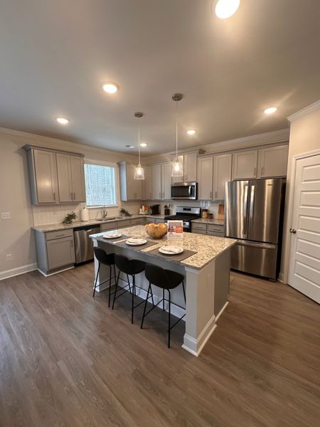 A modern kitchen with gray cabinets, granite countertops, a central island with seating, and stainless steel appliances.
