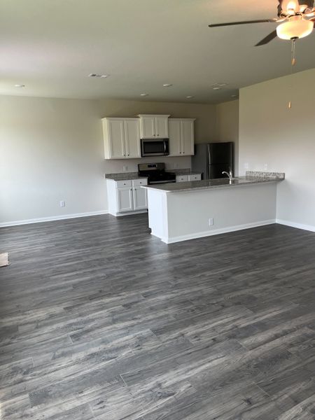 A modern kitchen with white cabinets, granite countertops, and sleek appliances adjacent to a spacious area with wood flooring.