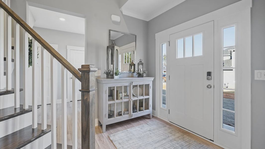 Two story entry with oak stairs, open railing, LVP flooring, lots of windows, and farm house decor at Village at Midway Two story entry with oak stairs, open railing, LVP flooring, lots of windows, and farm house decor at Village at Midway