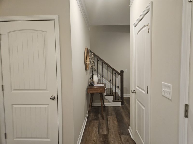 A warm hallway with wooden flooring, a small console table, and stairs with black metal railings leading to the upper floor.