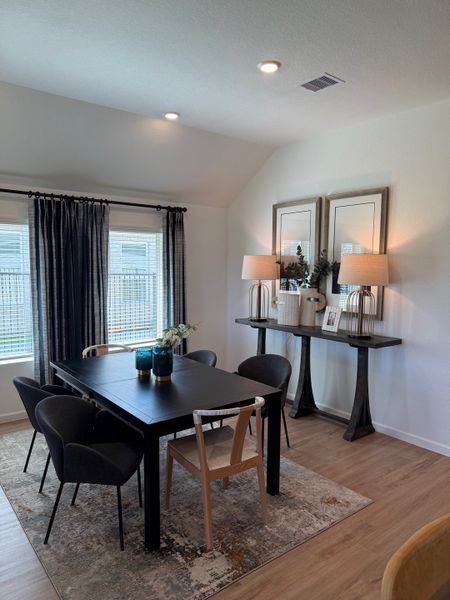 A modern dining room with a sleek black table, elegant chairs, and decorative mirrors, lit by contemporary lamps.