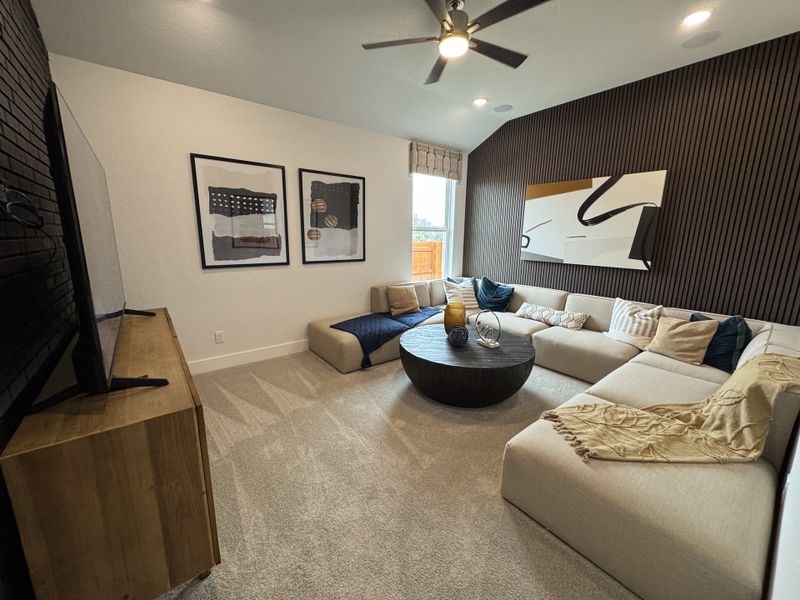 A cozy living room with a large sectional sofa, modern artwork, and a ceiling fan, ideal for relaxation and entertainment.
