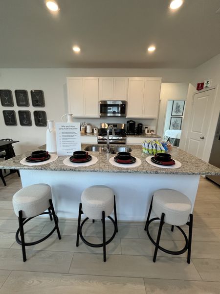 A modern kitchen with a sleek granite island, white cabinetry, and cozy stools, perfect for entertaining. A modern kitchen with a sleek granite island, white cabinetry, and cozy stools, perfect for entertaining.