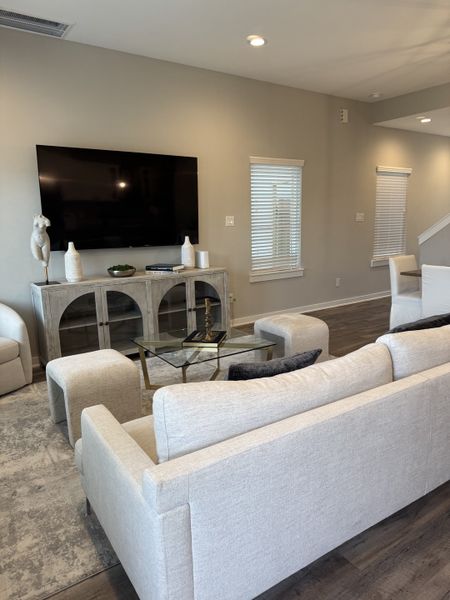 Modern living room with plush beige seating, glass coffee table, large TV, and neutral decor for an inviting ambiance.