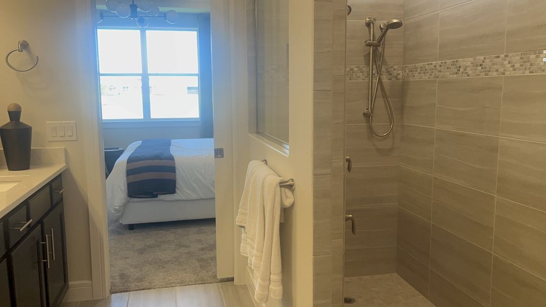 A modern bathroom with a spacious walk-in shower, elegant tile accents, and a plush adjoining bedroom.