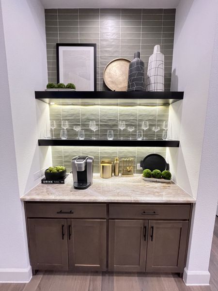 A chic coffee nook with marble countertop, black shelves, stylish decor, and modern cabinetry.