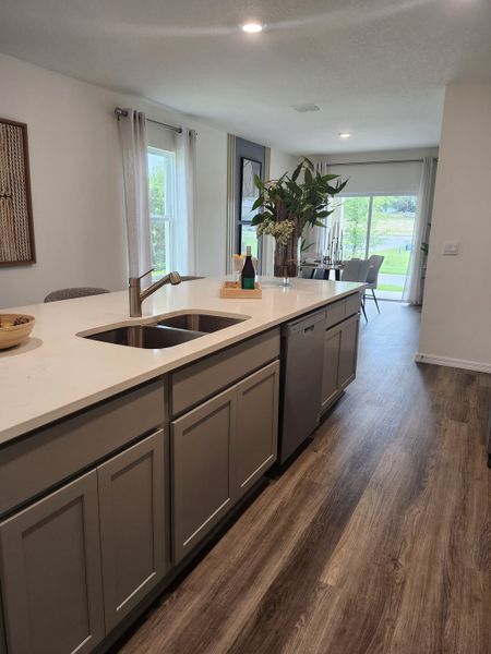 Modern kitchen with sleek grey cabinets, wood floors, and a bright dining area overlooking lush greenery.