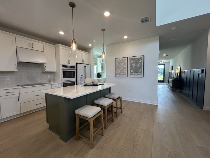 A modern kitchen with white cabinetry, pendant lighting, and a central island with seating. Open layout with stylish decor.