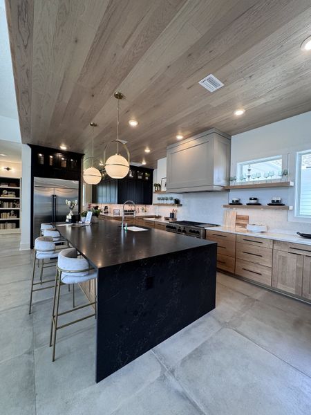 A modern kitchen with a black island, chic pendant lights, and wooden cabinetry, creating a stylish and functional space.