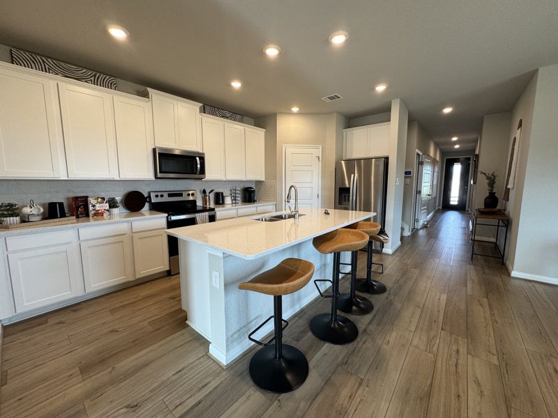 A modern kitchen with sleek white cabinets, a spacious island with stools, and stainless steel appliances.