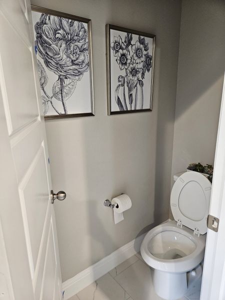 A cozy bathroom with framed botanical art, a sleek white toilet, and tile flooring. A cozy bathroom with framed botanical art, a sleek white toilet, and tile flooring.