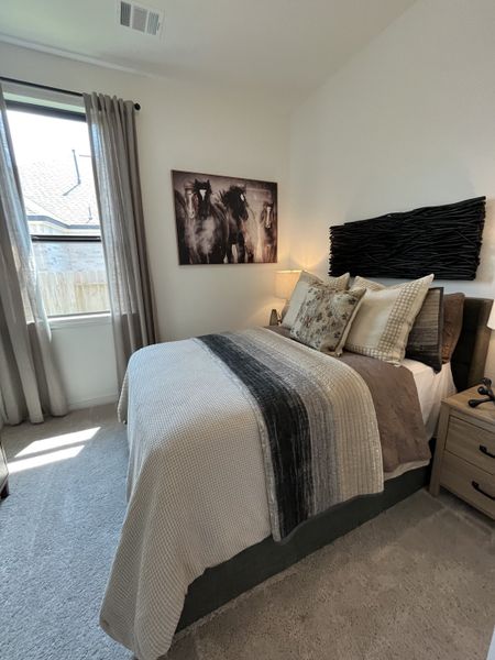 A cozy bedroom featuring a textured headboard, artful horse painting, and soft natural light from large windows. A cozy bedroom featuring a textured headboard, artful horse painting, and soft natural light from large windows.