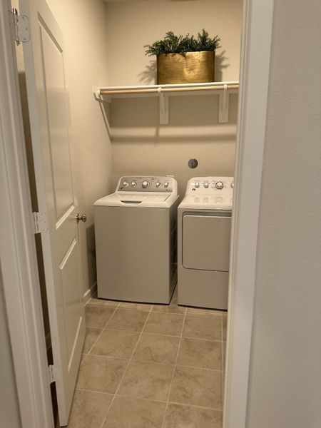 A functional laundry room with modern appliances, tile flooring, and a decorative plant on a shelf. A functional laundry room with modern appliances, tile flooring, and a decorative plant on a shelf.