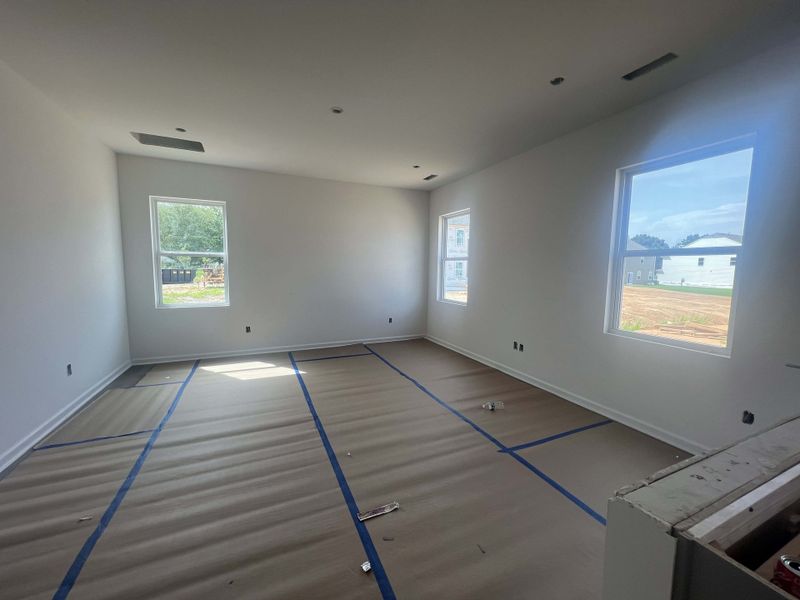 A sunlit room with three large windows, white walls, and protected flooring, ready for finishing touches.