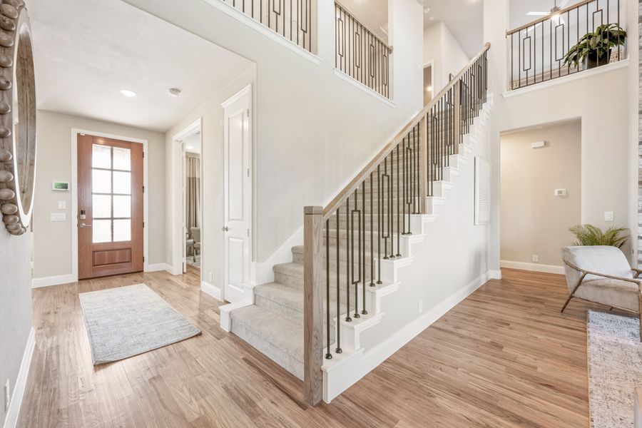 Two-story entryway with wood staircase, metal balusters, hardwood floors, and wood front door with glass panels Two-story entryway with wood staircase, metal balusters, hardwood floors, and wood front door with glass panels