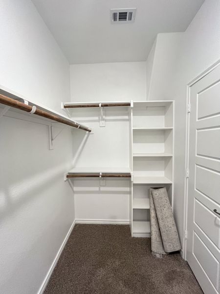A spacious walk-in closet with white shelving, hanging rods, and plush carpet for an organized storage solution. A spacious walk-in closet with white shelving, hanging rods, and plush carpet for an organized storage solution.