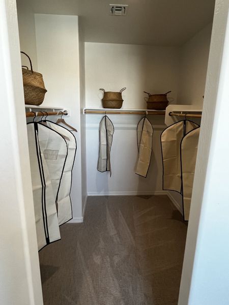 Spacious closet with hanging storage, baskets, and garment covers, featuring neutral tones and ample organization space.