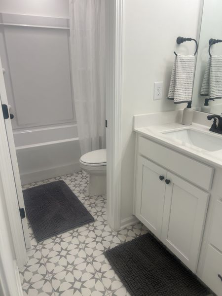 A modern bathroom with patterned tile flooring, white cabinetry, and dark fixtures. A modern bathroom with patterned tile flooring, white cabinetry, and dark fixtures.