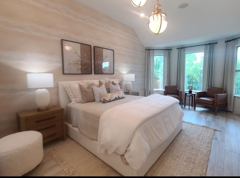 A serene bedroom with neutral tones, cozy bedding, elegant lighting, and large windows overlooking lush greenery.