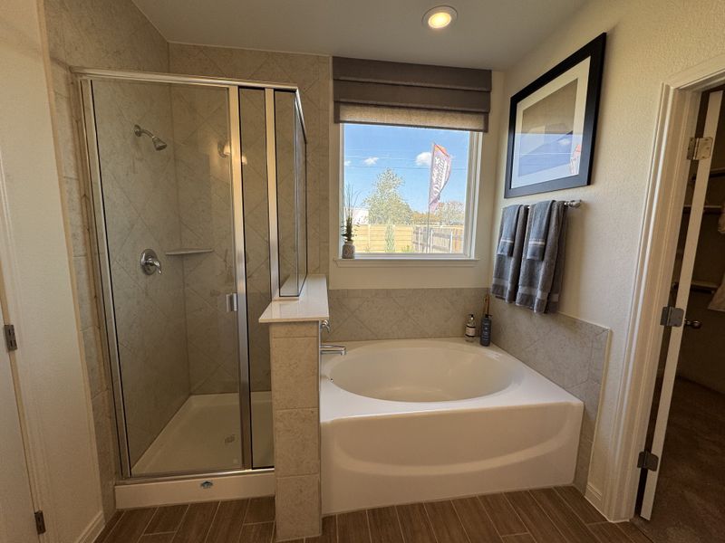A modern bathroom features a glass-enclosed shower, soaking tub, and natural light from a large window.