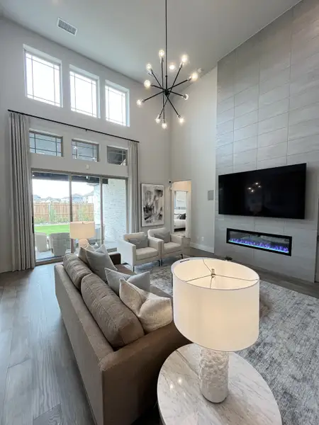 A modern living room with high ceilings, a sleek chandelier, large windows, and a cozy fireplace. A modern living room with high ceilings, a sleek chandelier, large windows, and a cozy fireplace.