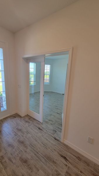 A bright room with wood-style tile flooring and glass sliding doors, leading to a sunny space with large windows.