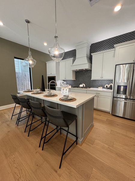A modern kitchen with sleek white cabinetry, patterned backsplash, pendant lights, and a spacious island with seating. A modern kitchen with sleek white cabinetry, patterned backsplash, pendant lights, and a spacious island with seating.