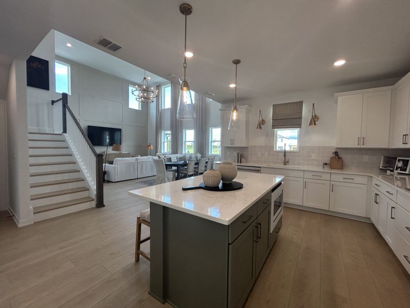 A spacious open-concept kitchen and living area with modern lighting, white cabinetry, and a large island.