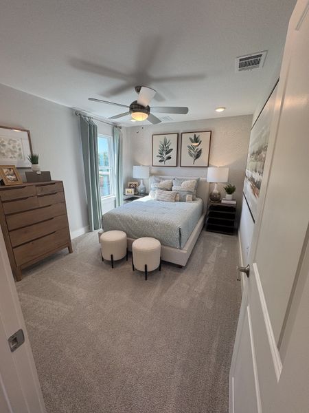 A cozy bedroom featuring a plush bed, elegant decor, wooden dresser, and modern ceiling fan.