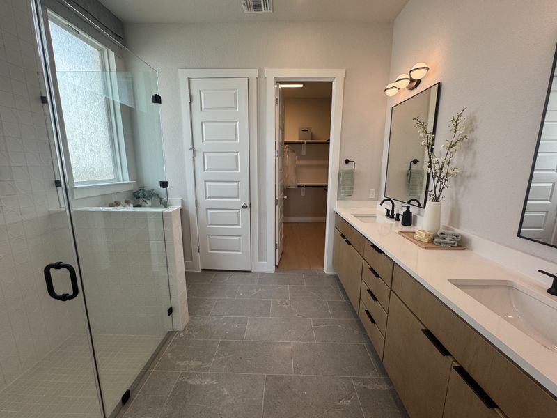 A spacious bathroom features a glass shower, dual sinks on a sleek vanity, and elegant gray tile flooring.
