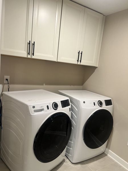 A functional laundry room with sleek white cabinets, modern washer, and dryer.