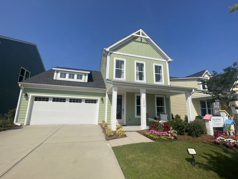 A charming green home with a welcoming porch and vibrant landscaping in Homecoming by True Homes (Ravenel, SC).