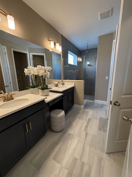 A sophisticated primary bathroom with dual sinks, gold fixtures, and a walk-in shower, blending elegance with functionality in Crossroads at Kelly Park by Dream Finders Homes (Apopka, FL).