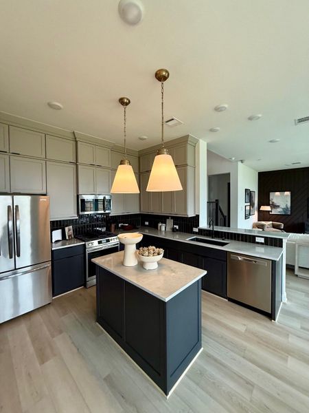 A modern kitchen with sleek cabinets, a central island, stainless steel appliances, and elegant pendant lighting.