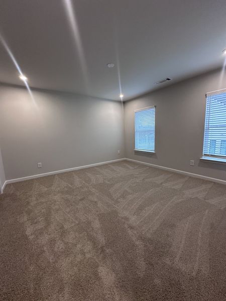 A spacious bedroom with soft carpeting, recessed lighting, and two windows for natural light.