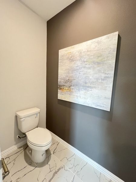 A sleek powder room featuring marble-tiled flooring, neutral walls, and modern artwork for a stylish touch.