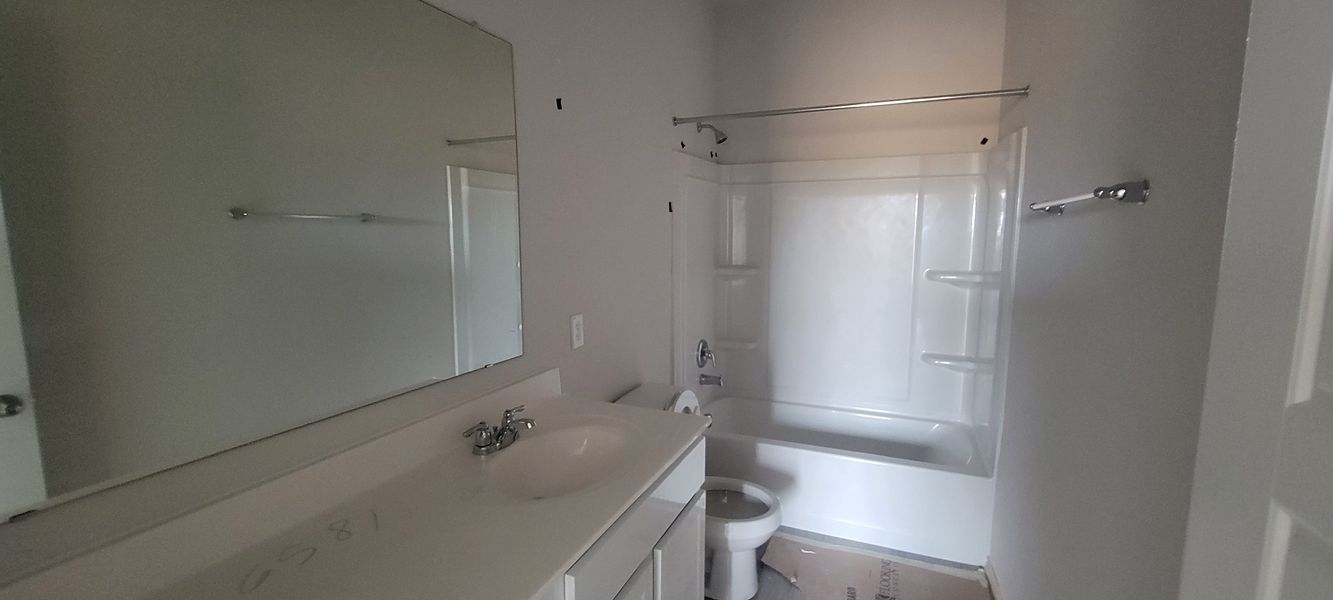 A clean, minimalistic bathroom with a white vanity, large mirror, and a shower-tub combination.