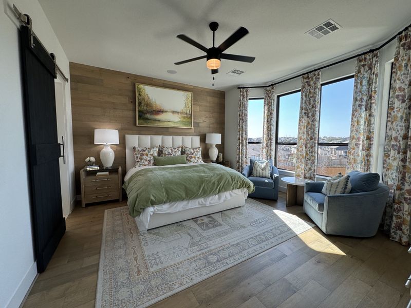 A cozy bedroom with a wood accent wall, plush bedding, and large windows draped in floral curtains. A cozy bedroom with a wood accent wall, plush bedding, and large windows draped in floral curtains.