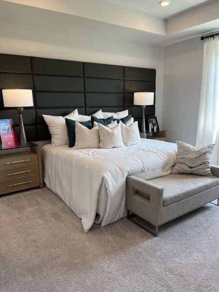 A cozy bedroom featuring a plush upholstered headboard, elegant lamps, and a chic bench, creating a serene retreat.
