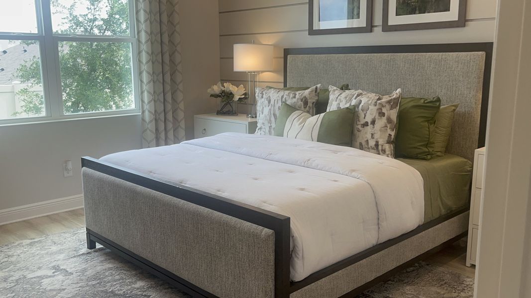 A cozy bedroom featuring a plush bed, elegant nightstand, and soft lighting with greenery views through the window.