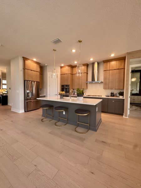 A modern kitchen with light wood cabinets, an island with stools, and elegant pendant lighting.